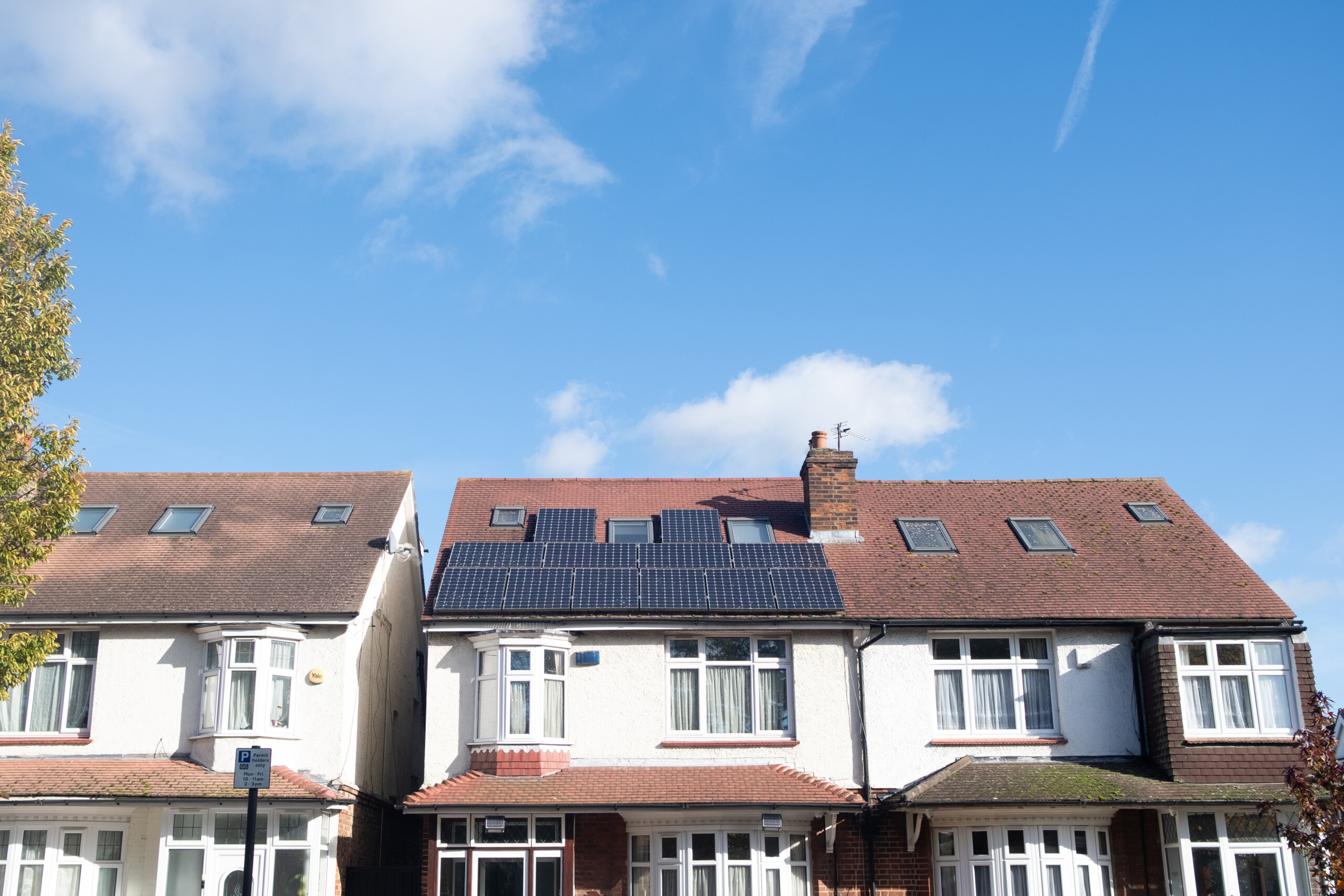 View of a row of British semi-detached homes under lots of blue sky. One house has solar panels on the roof.