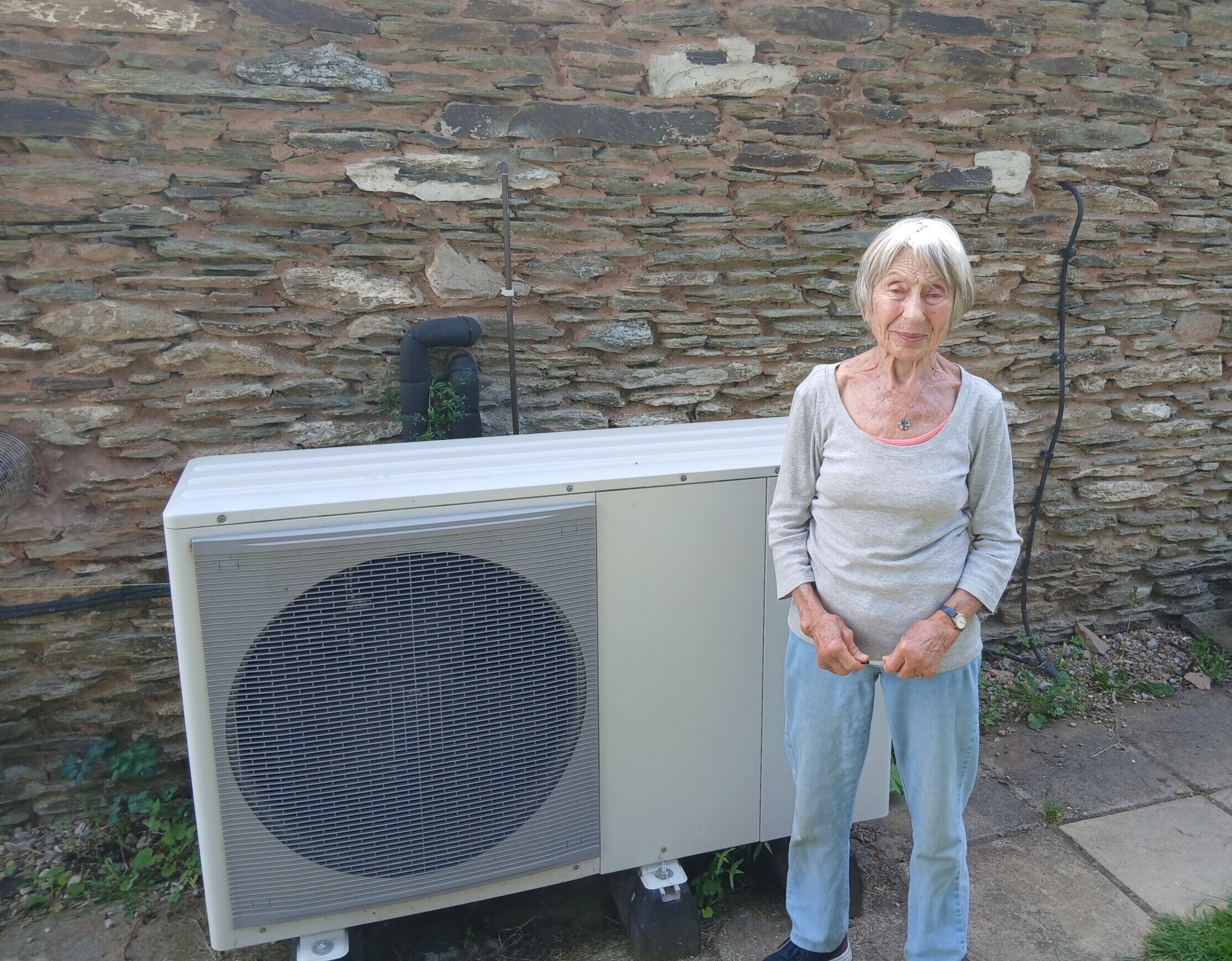 A woman stands in front of her heat pump.