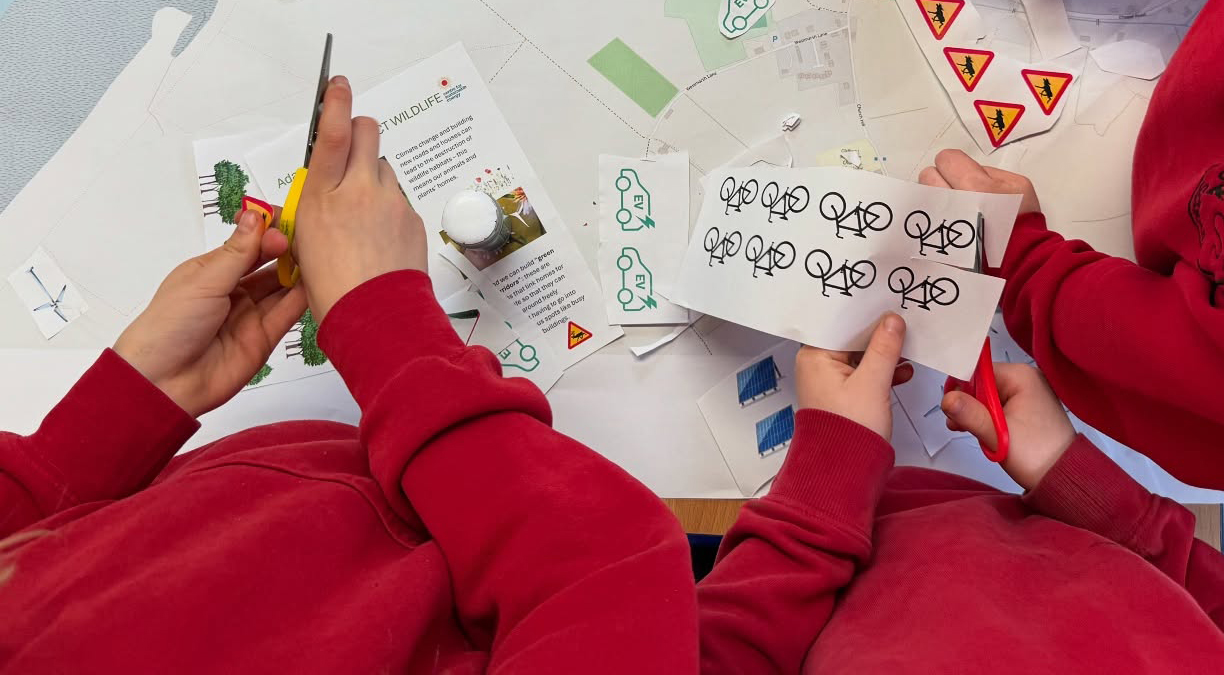 Primary school students cutting out pictures of bikes. Only their hands are visable.
