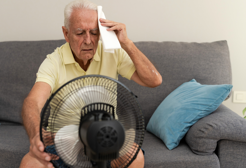 A man sitting by a fan wipes his brow