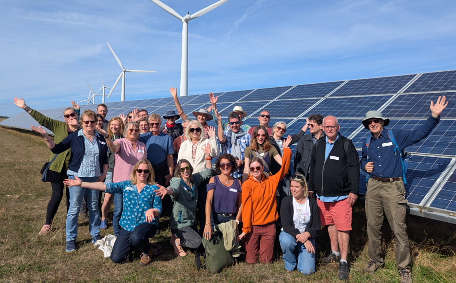 A group of around 25 celebrating people in front of wind turbines and solar panels.